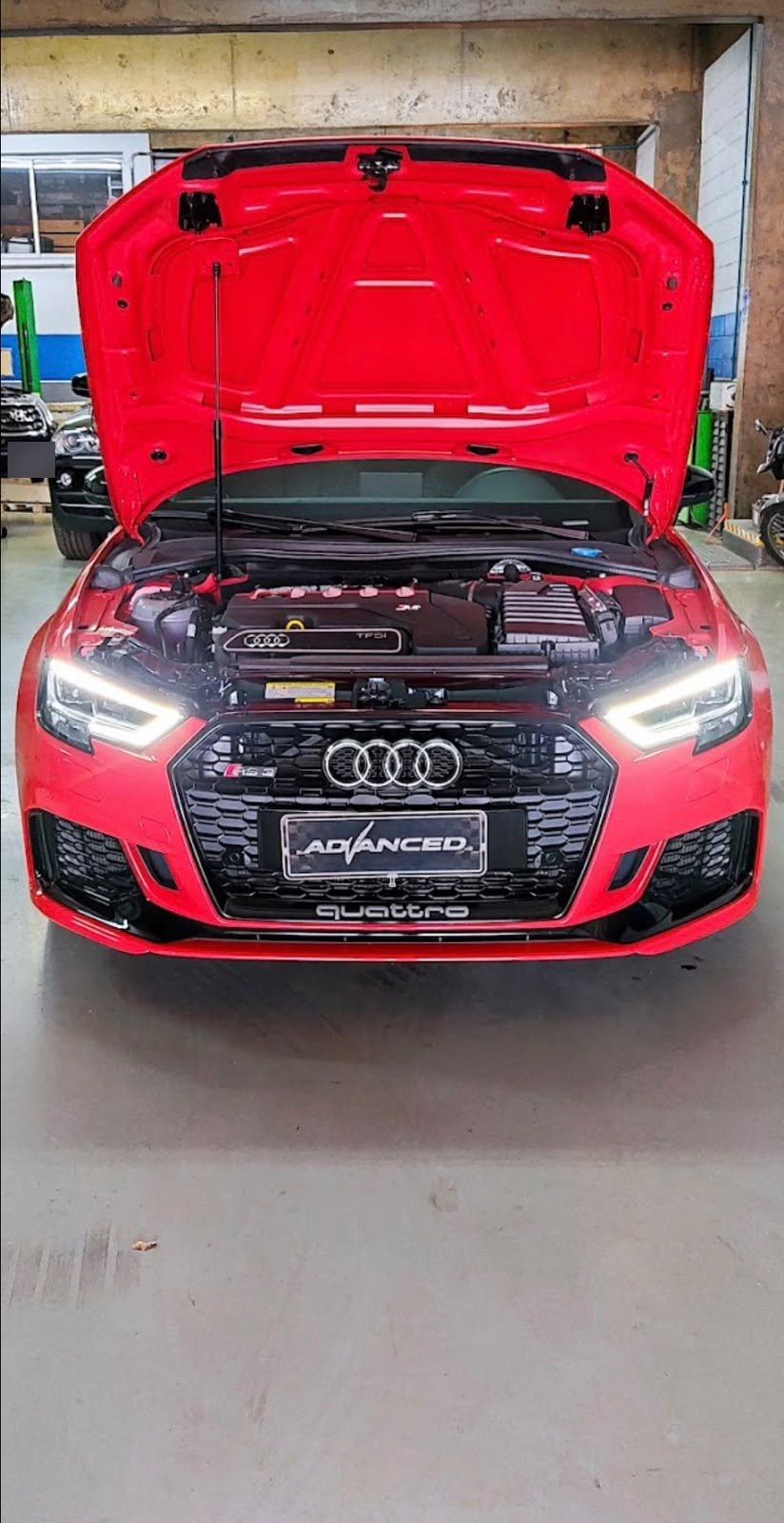 Audi vermelho com o capô aberto e a placa decorativa Advanced na grade dianteira.