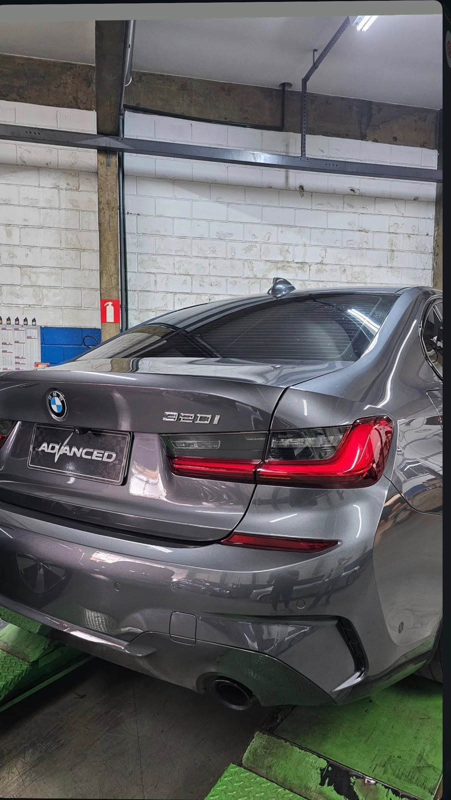 BMW 320i cinza sobre o elevador, com a placa decorativa Advanced na traseira.