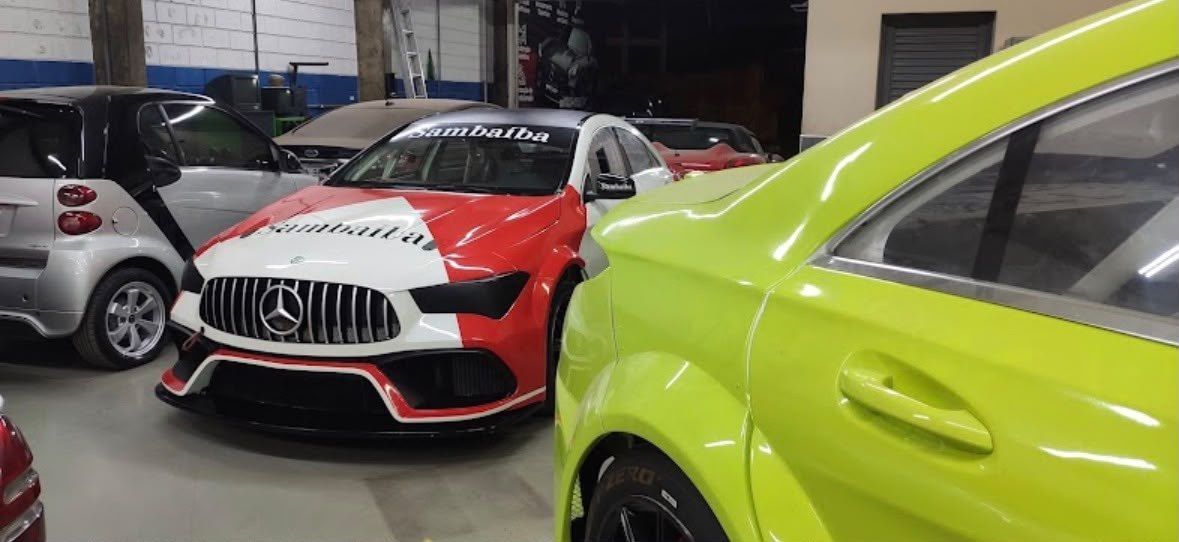 Carro de competição vermelho e branco e um carro verde-limão dentro da oficina.