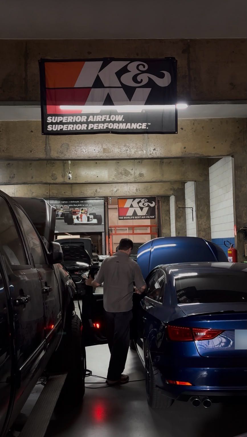 Interior da oficina com banner K&N, carros e um profissional ao fundo.